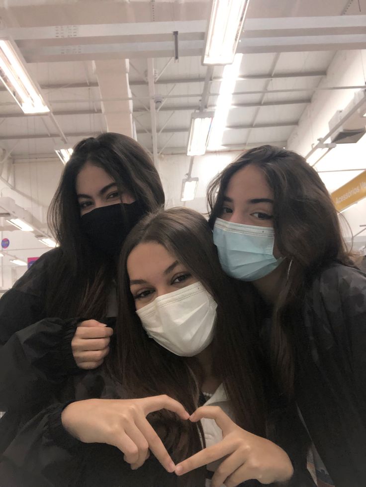 three girls wearing face masks and making the v sign with their hands in front of them