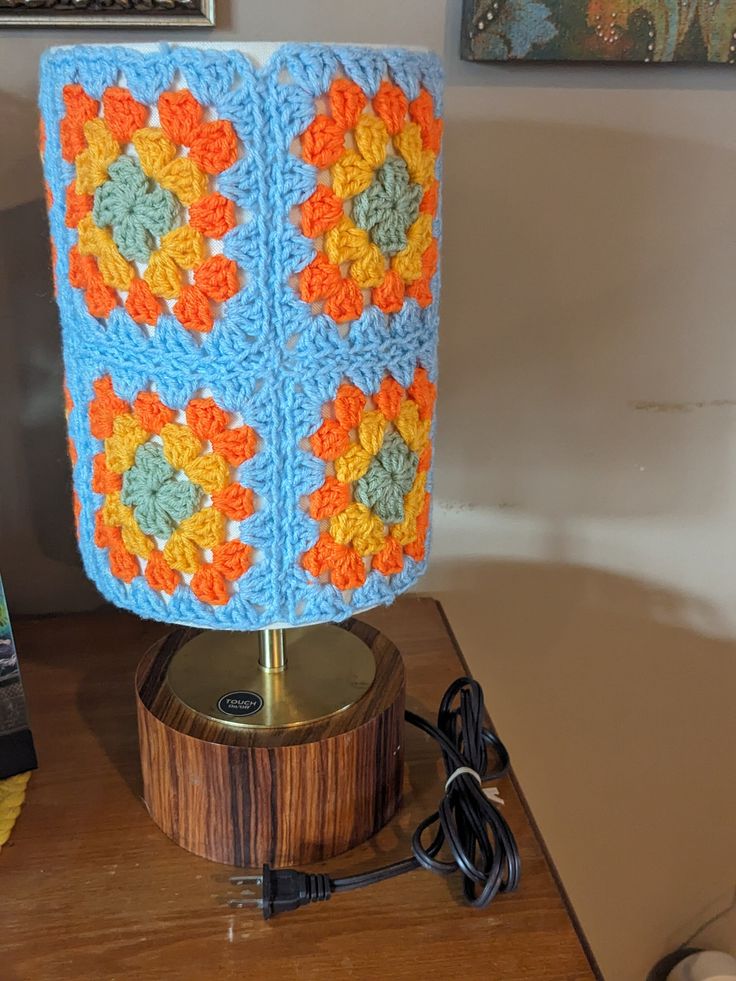 a crocheted lamp is sitting on a wooden table next to a cell phone