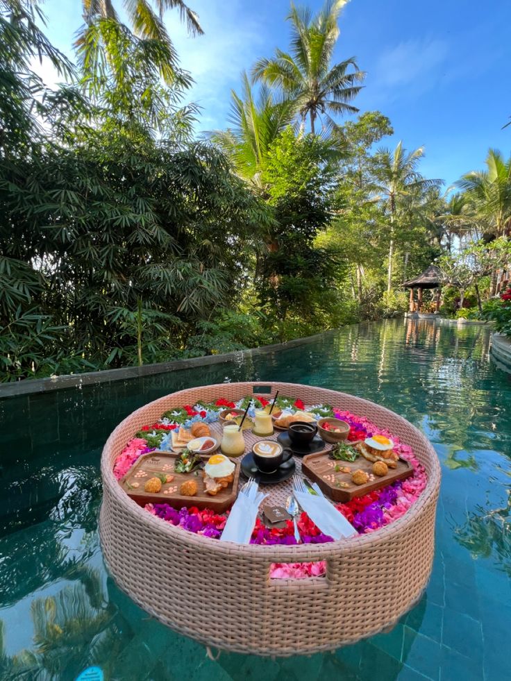 a picnic basket with food and drinks on the edge of a pool surrounded by palm trees