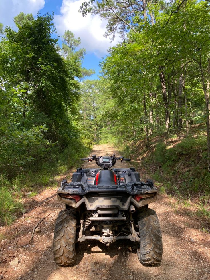 a four - wheeler is parked on a dirt road in the middle of some trees