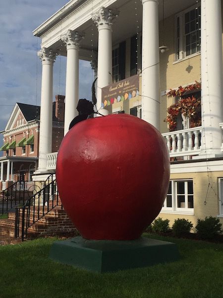 a large red apple sitting on top of a green block in front of a building