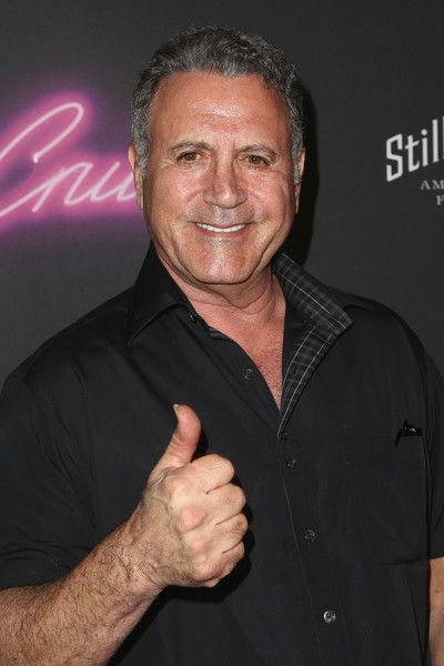 a man giving the thumbs up sign in front of a black wall with neon signs on it