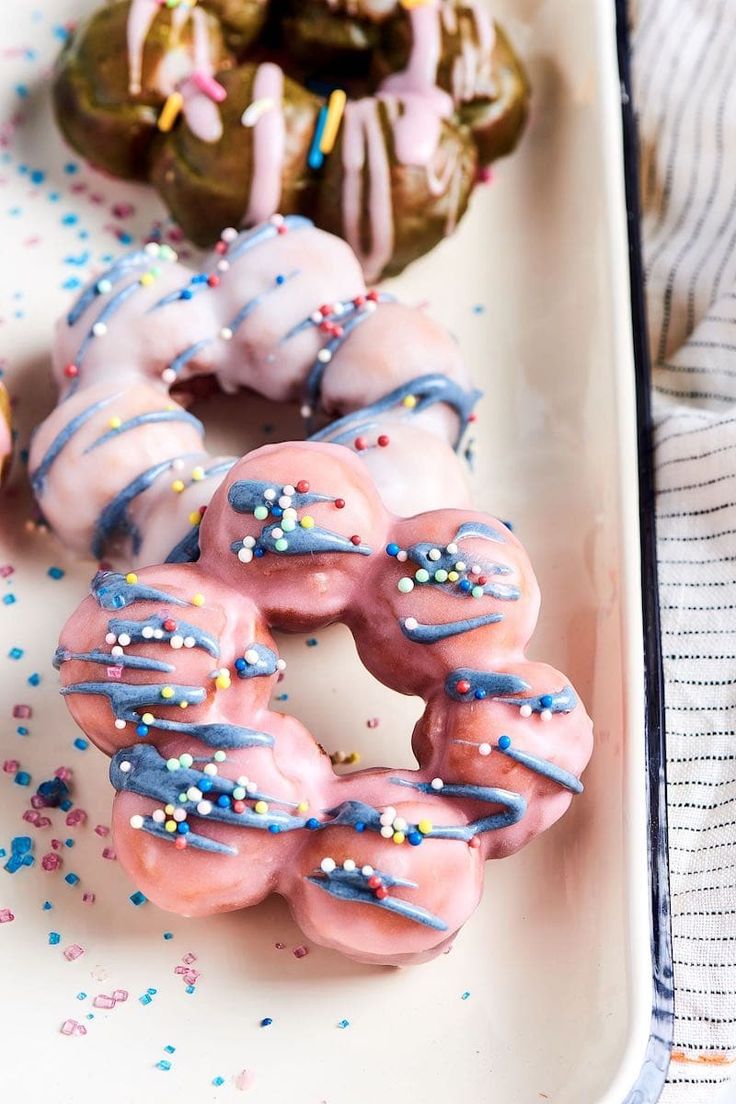 three donuts with sprinkles are on a white plate next to other donuts