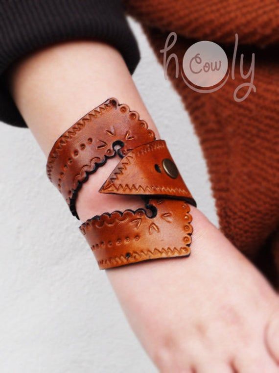 a woman wearing a brown leather bracelet with an intricate design on it's wrist