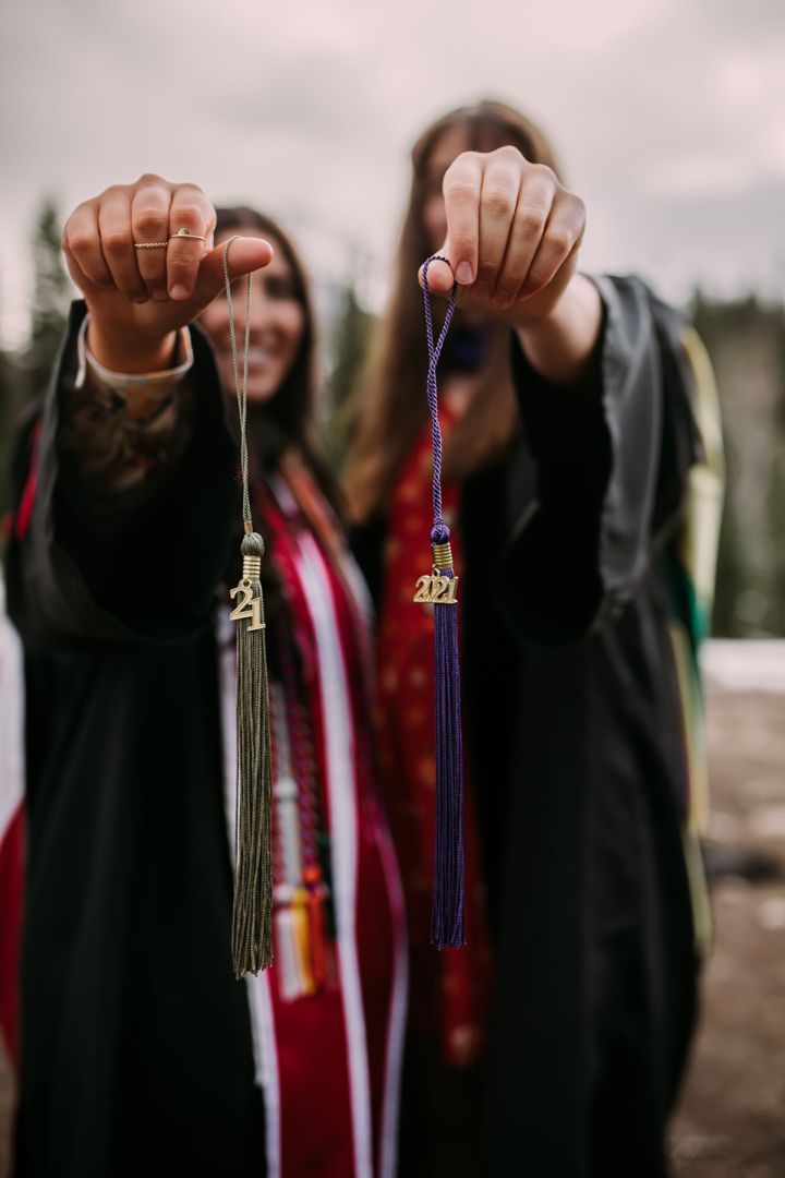 two women wearing graduation gowns hold up their tassels