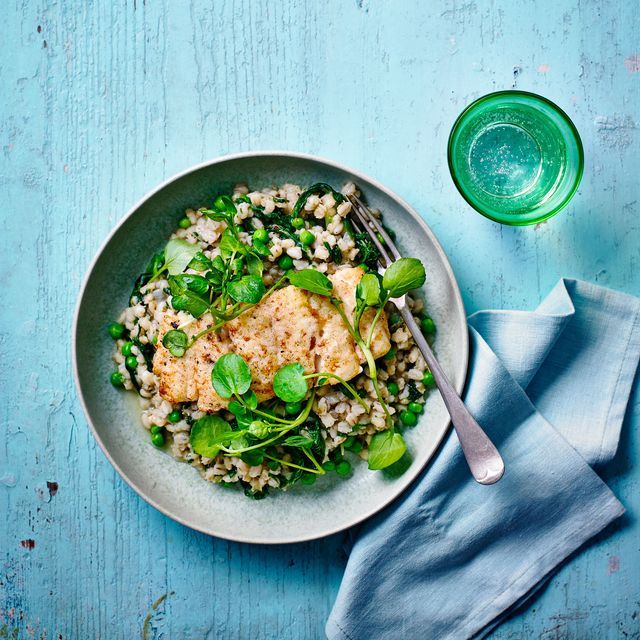 a white plate topped with rice and greens next to a glass of green water on top of a blue wooden table