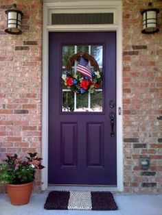 a purple front door with wreaths and potted plants