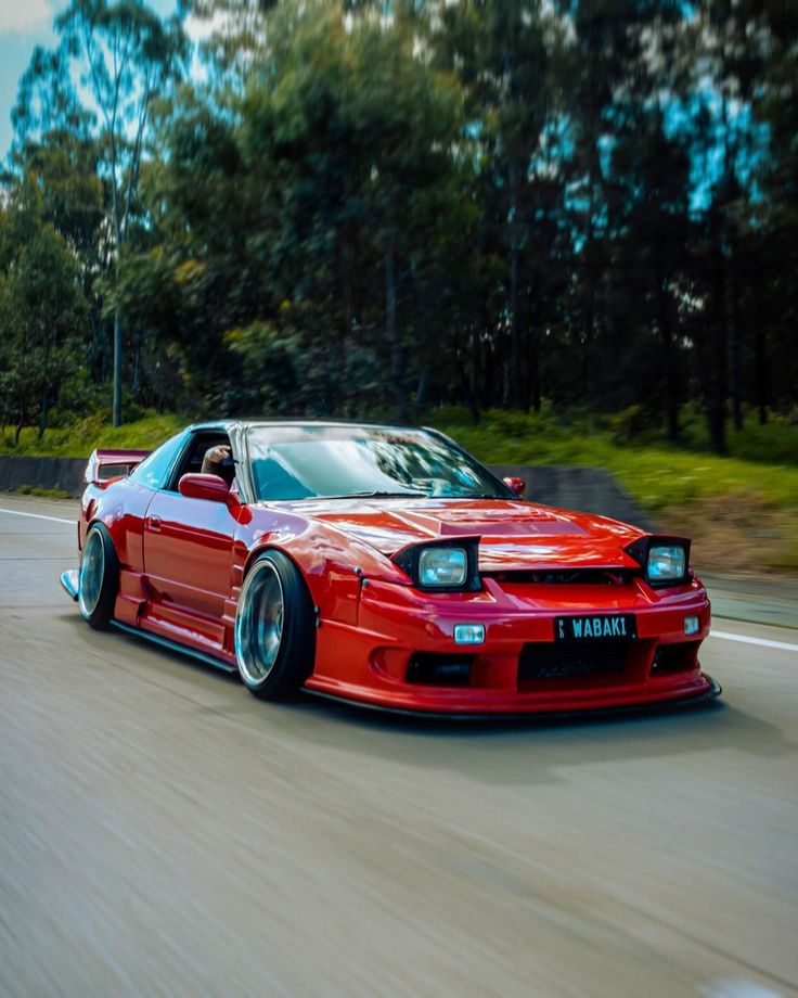 a red sports car driving down the road with trees in the backgrouund