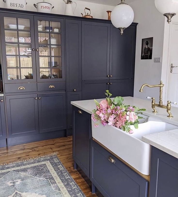 a kitchen with dark blue cabinets and white counter tops, gold faucets and pink flowers on the sink