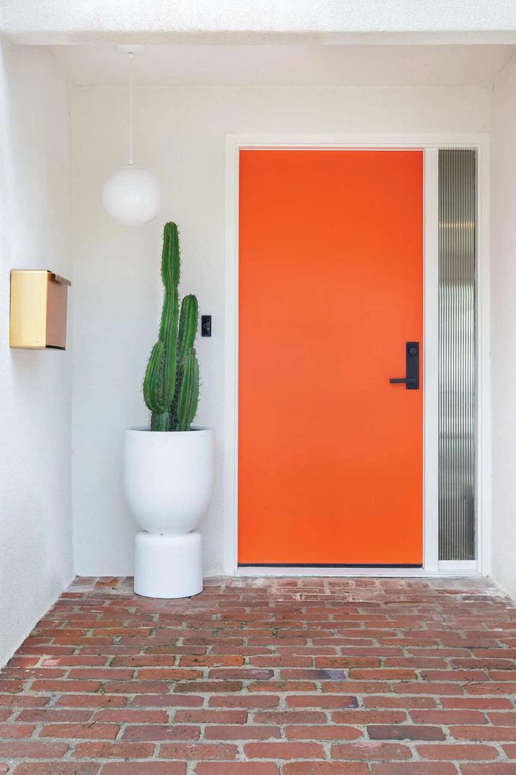 an orange door and white planter in front of a red brick wall with two lights