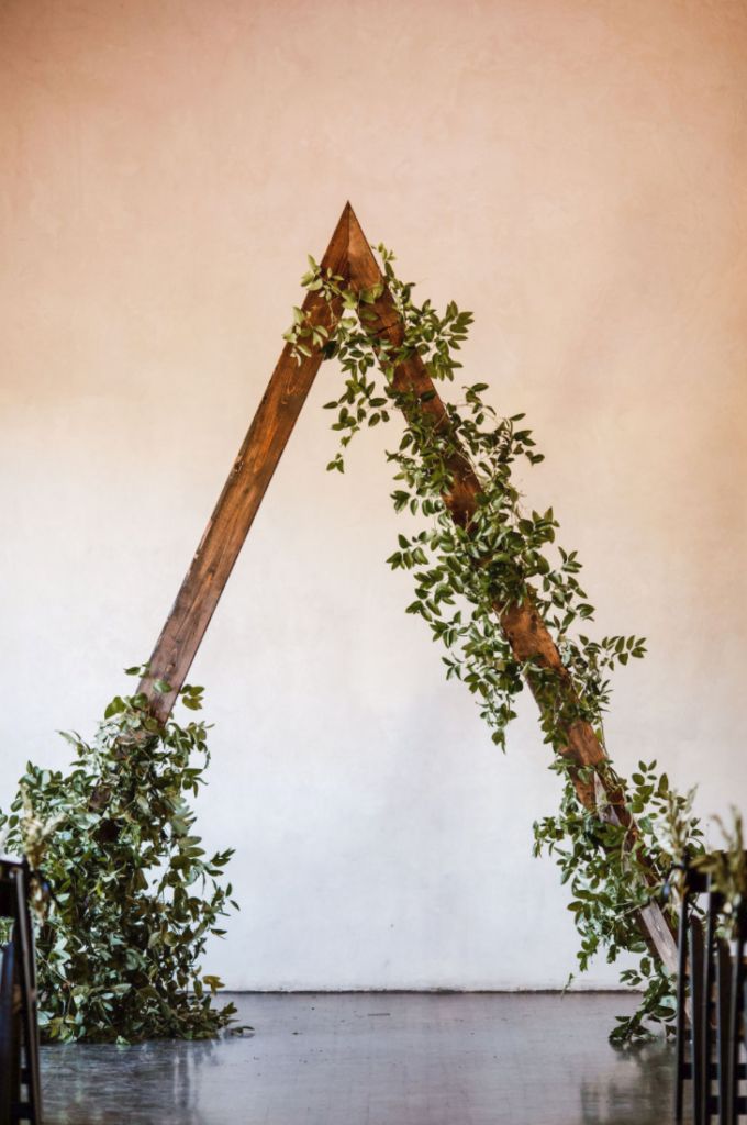 an arch made out of wooden sticks and greenery on the floor in front of a wall