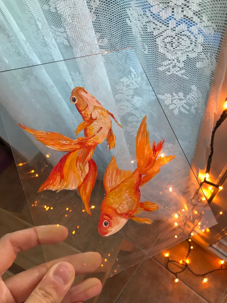 two goldfish in a clear glass bowl with lights on the wall and behind them