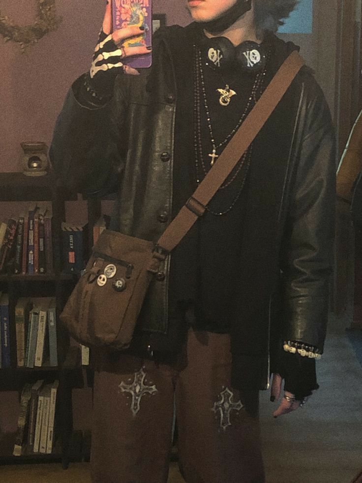 a man in black jacket and brown pants holding up a cell phone while standing next to a bookshelf