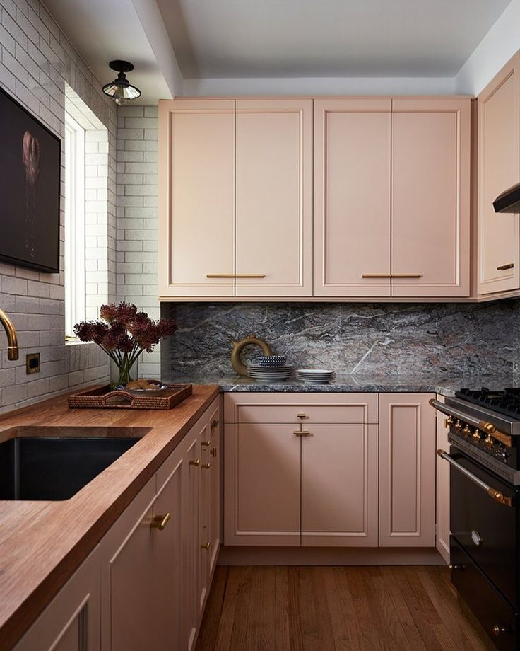 a kitchen with pink cabinets and marble counter tops, along with a black stove top oven