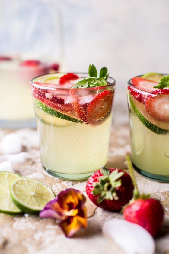 two glasses filled with drinks sitting on top of a table next to strawberries and limes