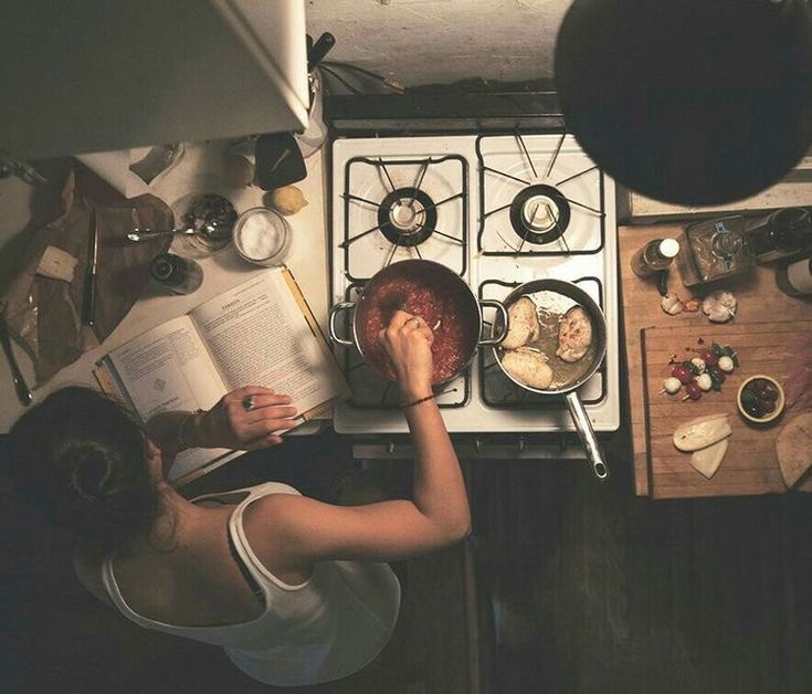 a woman is reading a book while cooking in the kitchen with an open cookbook