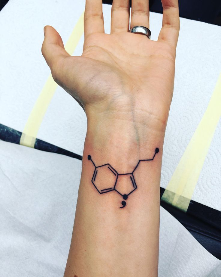 a person's hand with a black ink tattoo on their left wrist and the outline of a hexagonal structure