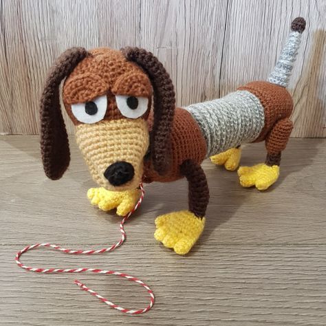 a crocheted dog with big eyes and long legs on a wooden floor next to a rope