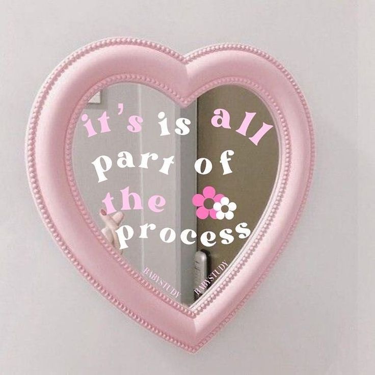 a pink heart shaped mirror hanging on the wall with words written in it's center