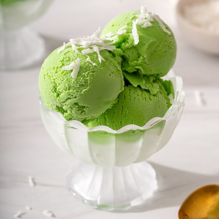 three scoops of green ice cream in a glass bowl on a white tablecloth