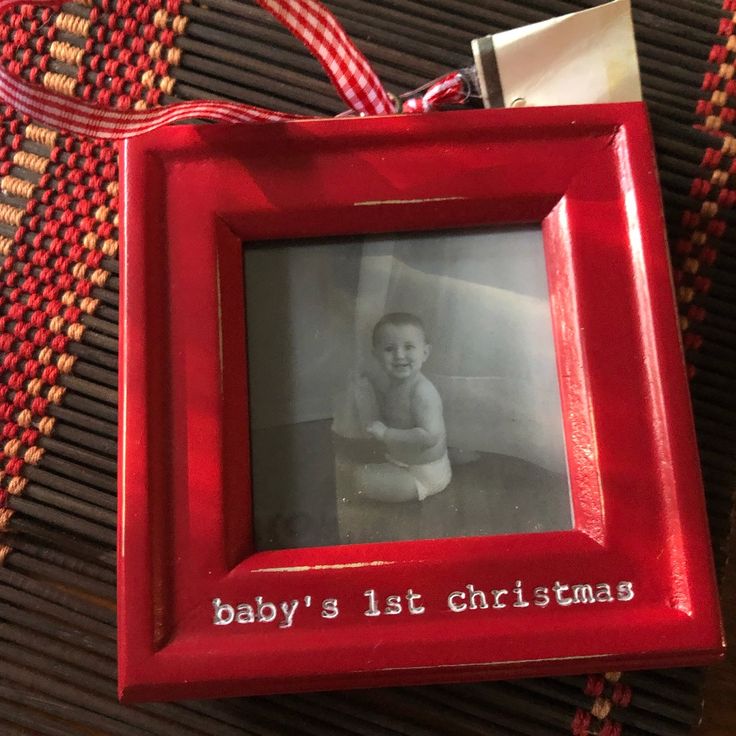 a baby's first christmas ornament hanging from a red frame on a table