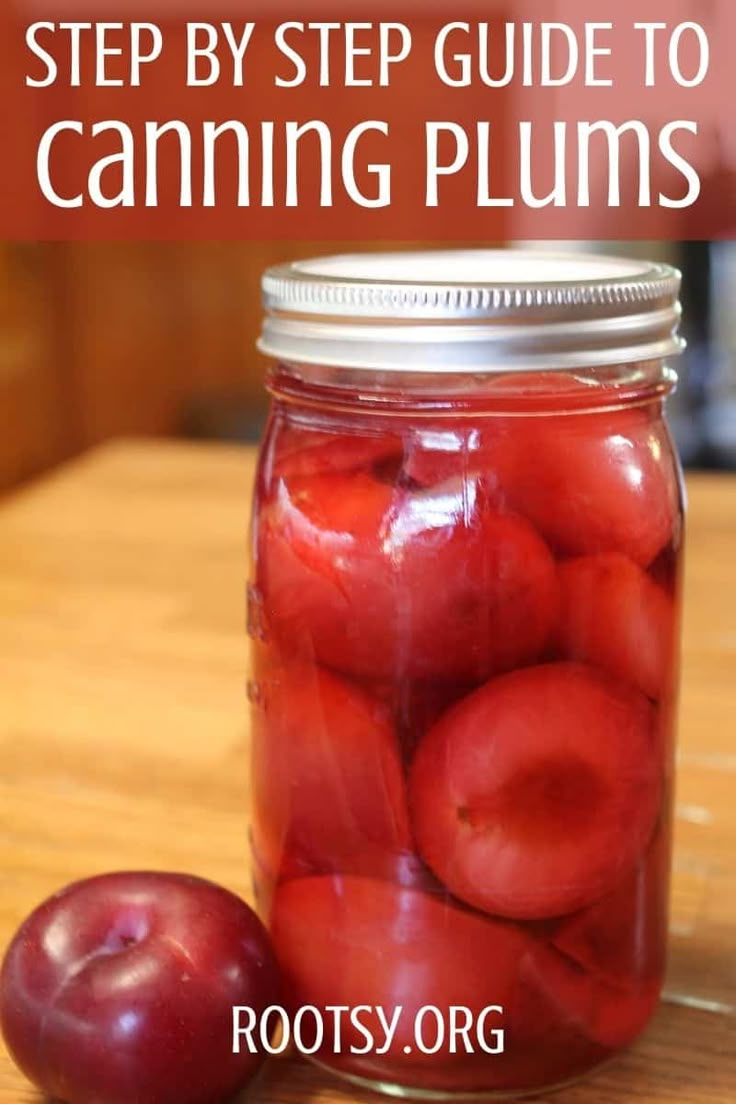 a jar filled with red plums sitting on top of a wooden table next to an apple