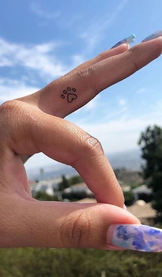 a person's hand with a small dog paw tattoo on their thumb and finger