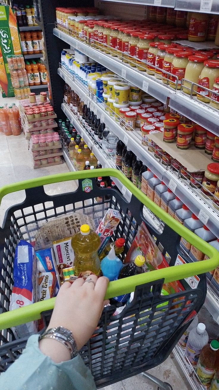 a person pushing a shopping cart through a grocery store filled with food and condiments