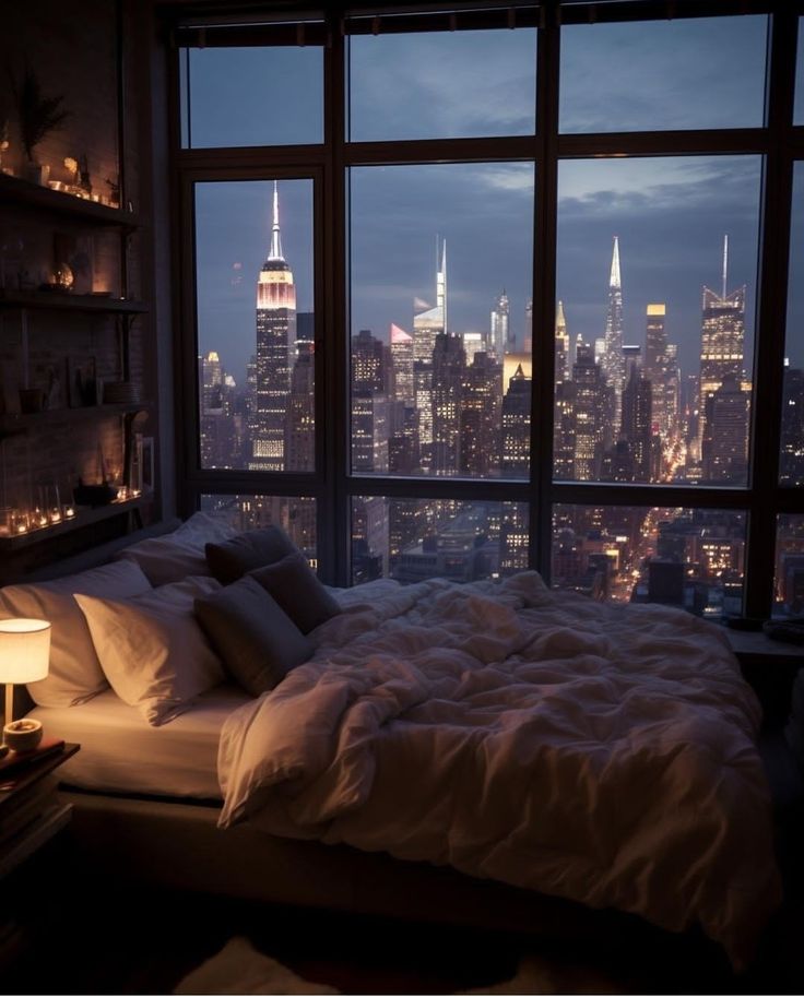 a bedroom with a large window overlooking the city lights and skyscrapers are lit up at night