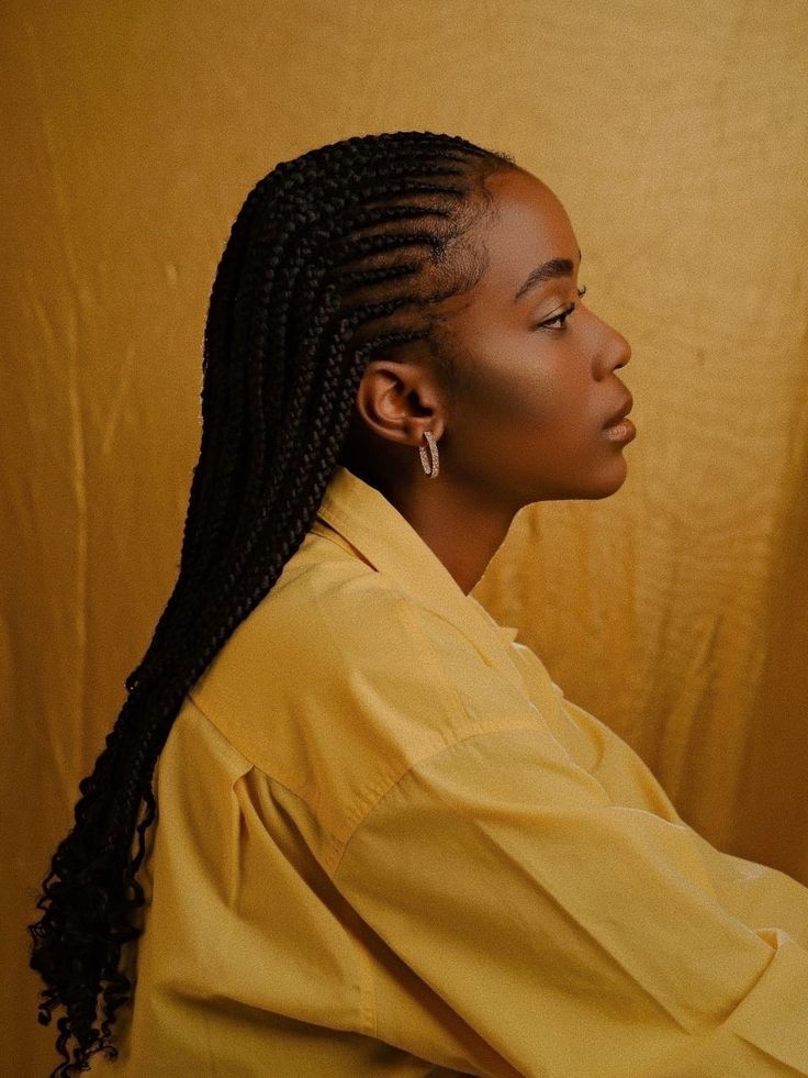 a woman with braids sitting in front of a yellow wall and looking off to the side