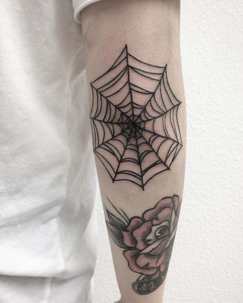 a person with a spider web tattoo on their arm holding a pink rose in front of them