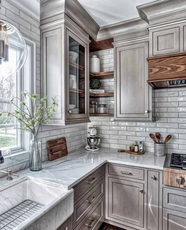 a kitchen with gray cabinets and white marble counter tops is pictured in this image, there are plants on the window sill