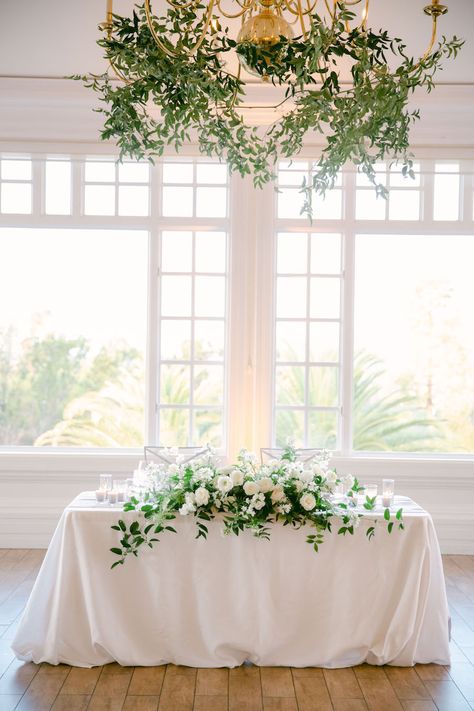 a table with white flowers and greenery on it in front of a chandelier