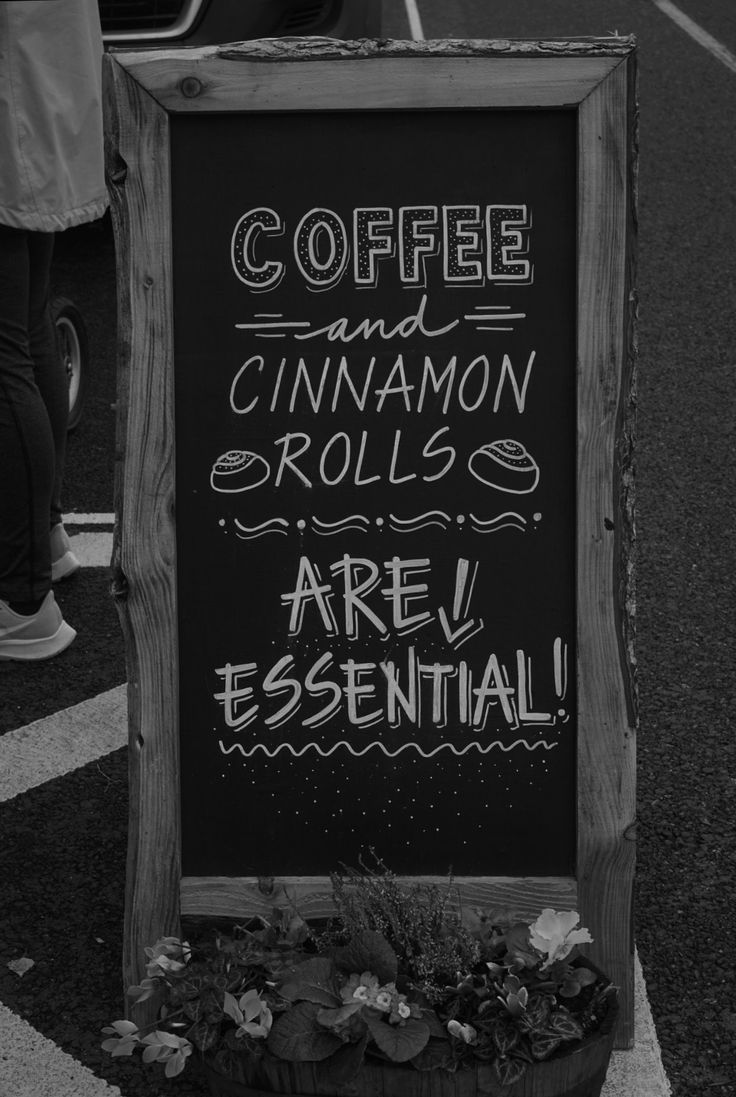 a chalkboard sign with coffee and cinnamon rolls written on it in front of people