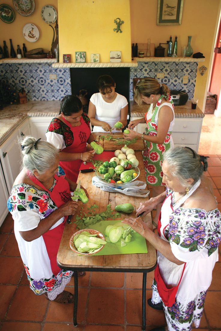 several women are standing around a table with vegetables on it and cutting them into small pieces