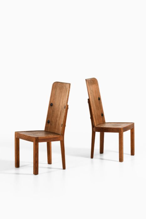 two wooden chairs sitting next to each other on a white surface with one chair facing the other