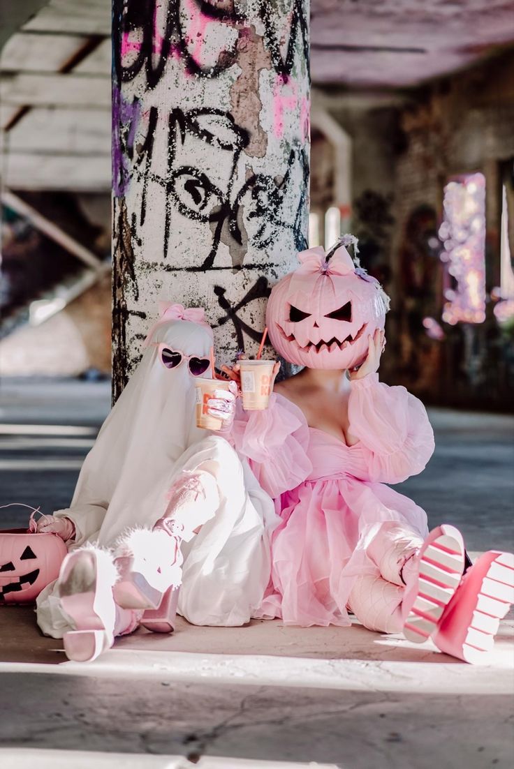 two creepy dolls sitting next to each other on the ground near a tree and graffiti covered wall