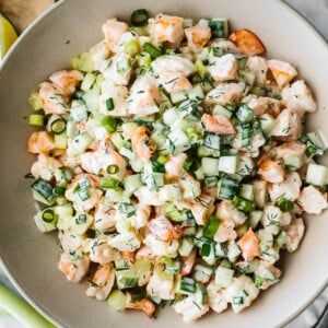 a white bowl filled with shrimp salad next to lemons and celery wedges