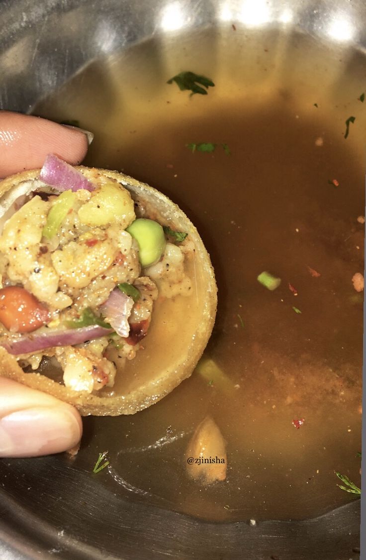 a person is holding a tortilla filled with vegetables and sauce in a pot