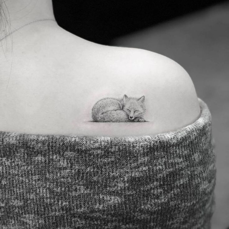 a black and white photo of a woman's shoulder with a small fox tattoo on it