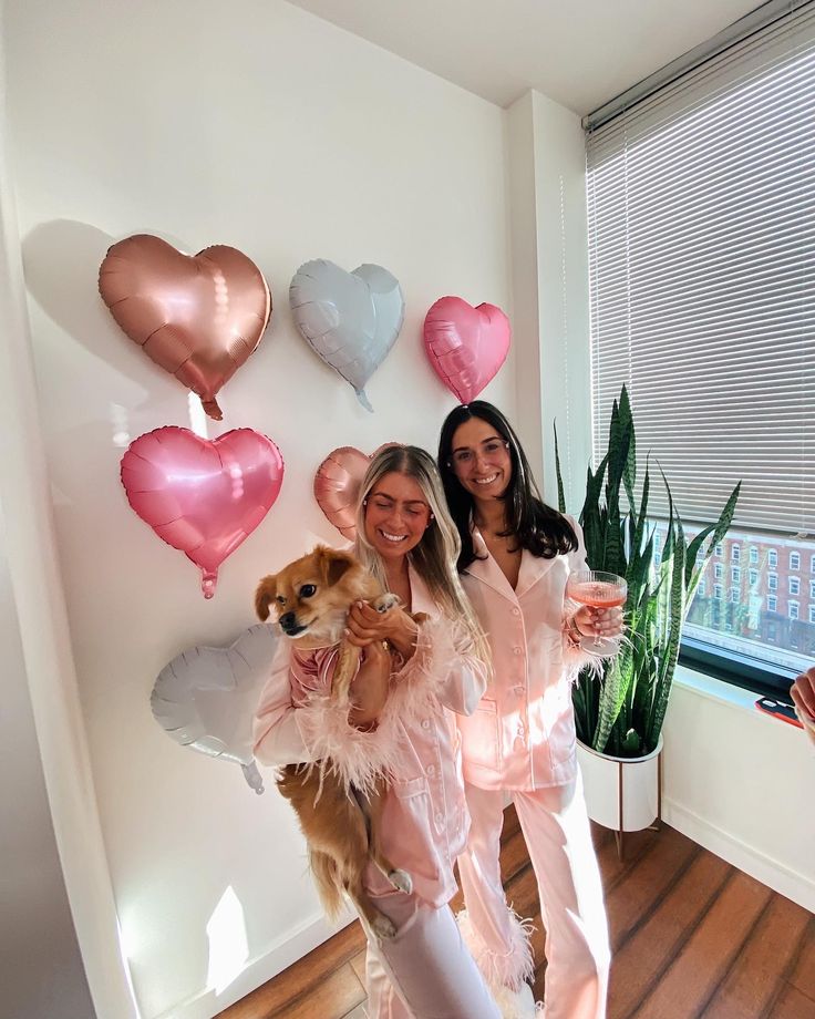 two women standing next to each other with balloons on the wall behind them and a dog