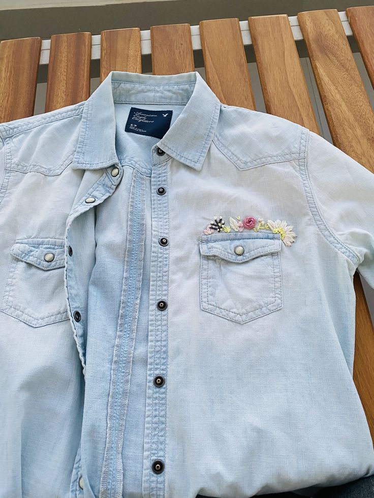 a blue jean shirt with flowers on the chest and two small patches in the pocket