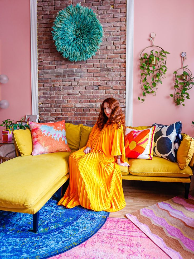 a woman in an orange dress sitting on a yellow couch next to a brick wall