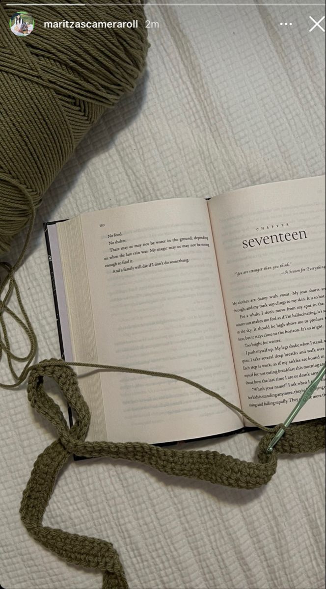 an open book on top of a bed next to a ball of yarn