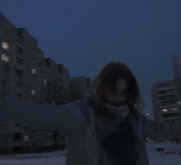 a woman standing in the snow with her arms spread out and buildings lit up behind her