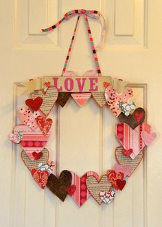 a heart shaped wreath hanging on a door with the word love spelled in pink and brown