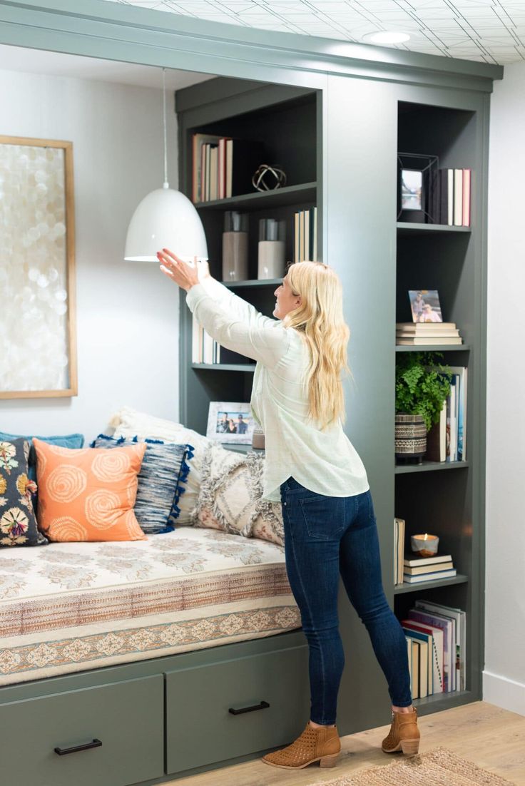 a woman is reaching for something on the book shelf in front of her bed and bookshelf