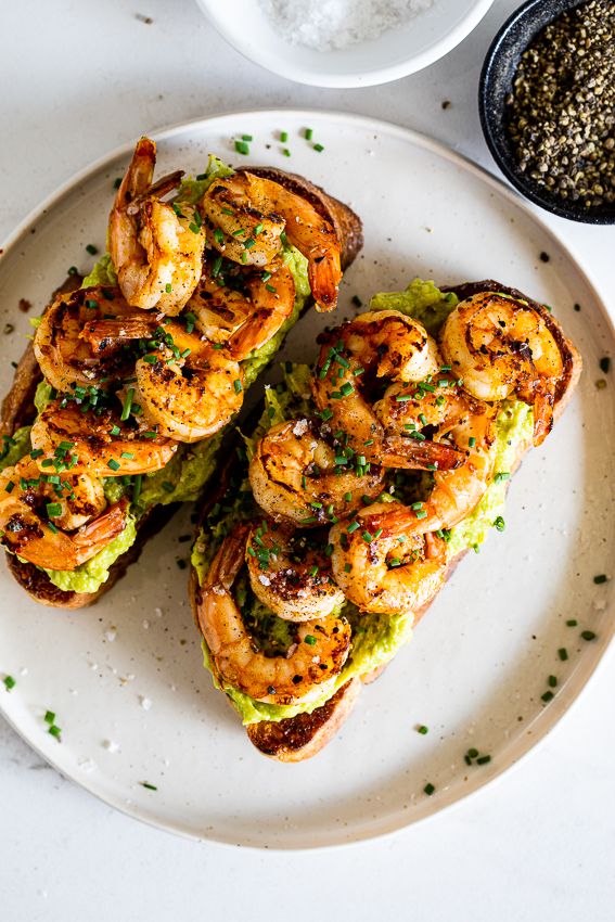 grilled shrimp and avocado sandwiches on a white plate next to salt and pepper