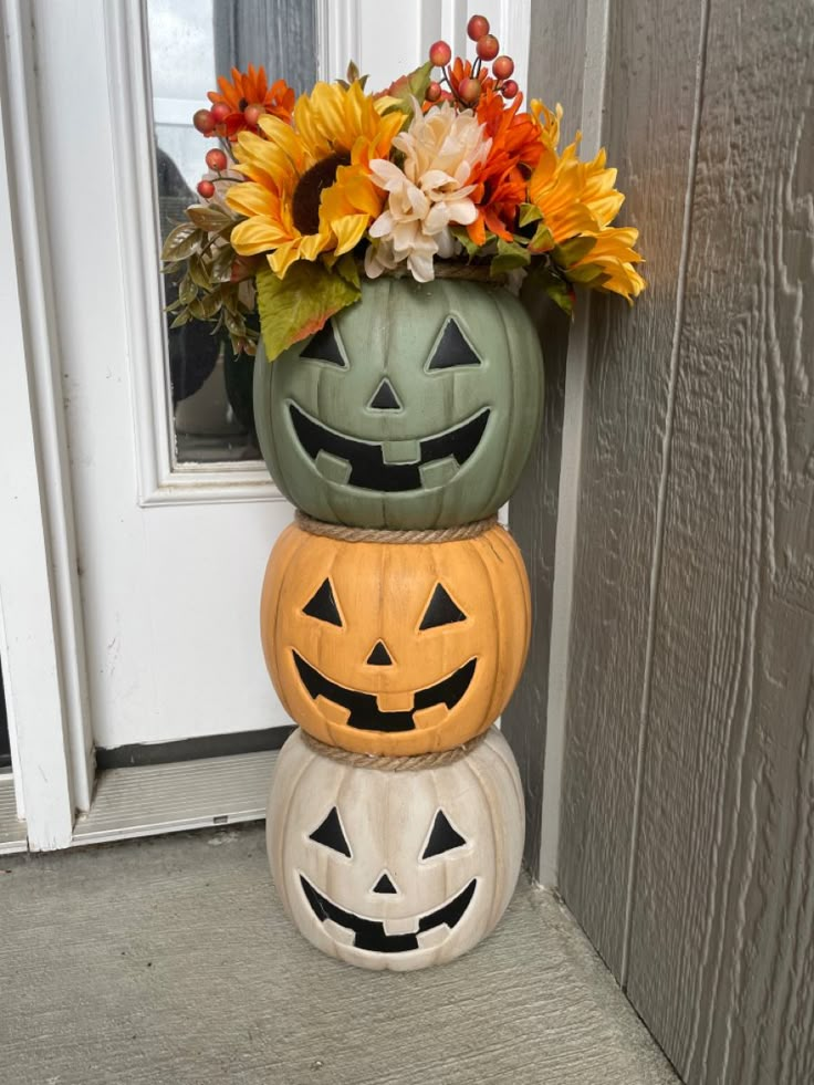 three pumpkins stacked on top of each other in front of a door with flowers