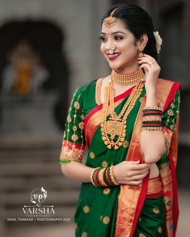 a woman in green and red sari with gold jewelry on her neck, smiling at the camera